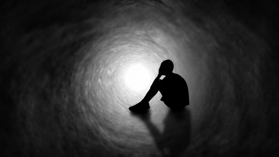 Figura solitaria seduta in un tunnel oscuro, simbolo di isolamento emotivo e solitudine